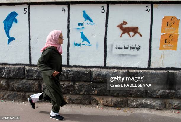 Moroccan woman walks past a wall on which are painted the symbols of the political parties running for the parliamentary elections in the Moroccan...