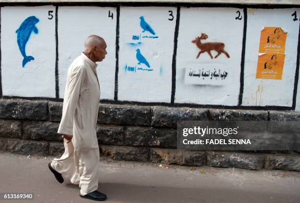 Moroccan man walks past a wall on which are painted the symbols of the political parties running for the parliamentary elections in the Moroccan...