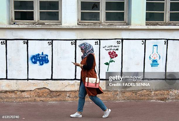 Moroccan woman walks past a wall on which are painted the symbols of the political parties running for the parliamentary elections in the Moroccan...
