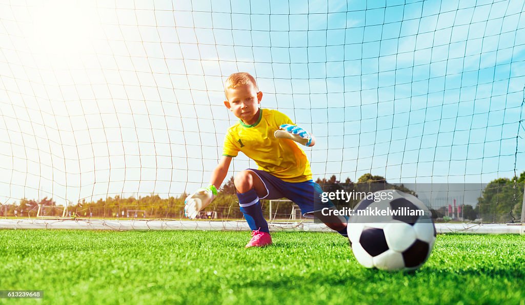 ゴールキーパージャンプし、サッカーボールをブロックしようとします