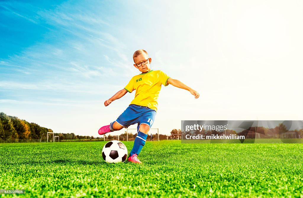 Boy plays soccer on field and kicks football