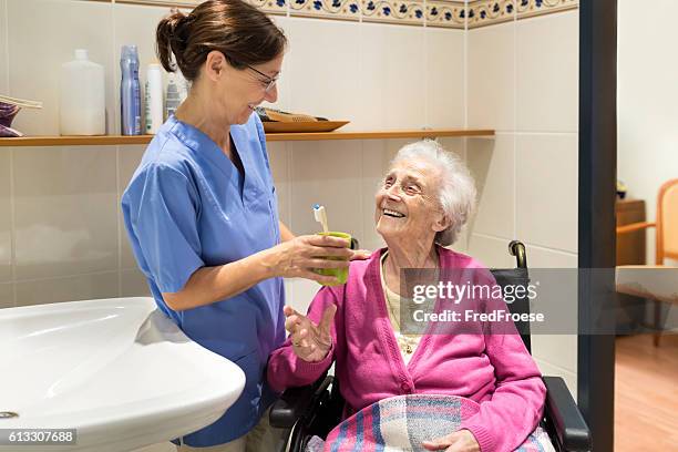 home caregiver mit seniorin im badezimmer - dental care stock-fotos und bilder