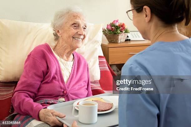 häuslicher betreuer mit senior erwachsenen frau, serviert eine mahlzeit - spitalbett stock-fotos und bilder