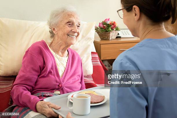 home caregiver with senior adult woman, serving a meal - nurse helping old woman at home stockfoto's en -beelden
