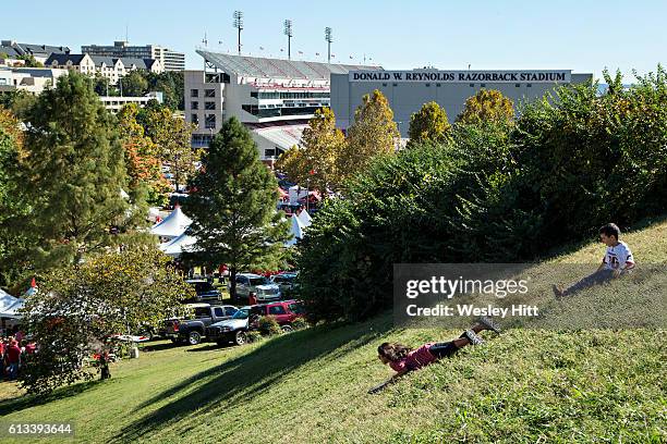 Kids slide down a grassy hill in view of the stadium before a game between the Arkansas Razorbacks and the Alabama Crimson Tide at Razorback Stadium...