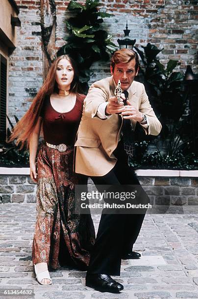 Quintessentially English actor Roger Moore and English actress Jane Seymour pose for an action shot during the filming of the 1973 James Bond film...