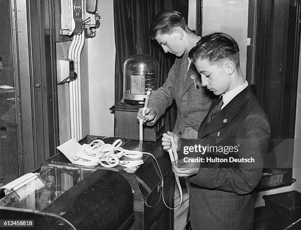 Two boys read confirmation of the D-Day invasion from the tape machine in a Fleet Street newspaper office.