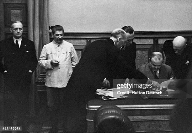 Soviet Foreign Minister signs the Nazi-Soviet Nonaggression Pact in the Kremlin. Stalin and Foreign Minister Ribbentrop of the Third Reich look on.