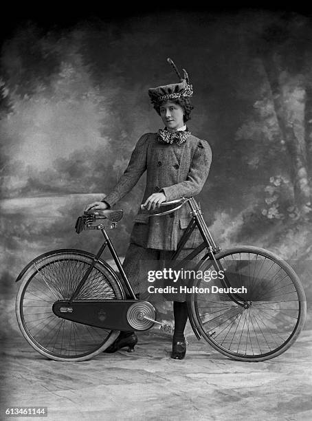 Victorian lady wearing plus fours poses beside her bicycle.