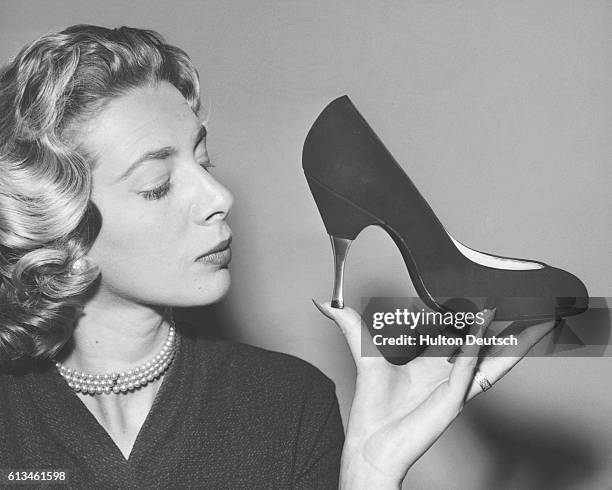 Model holds an aluminium-heeled, stiletto shoe, made with black suede, at a show of Dolcis' autumn collection. Mayfair, 1956.