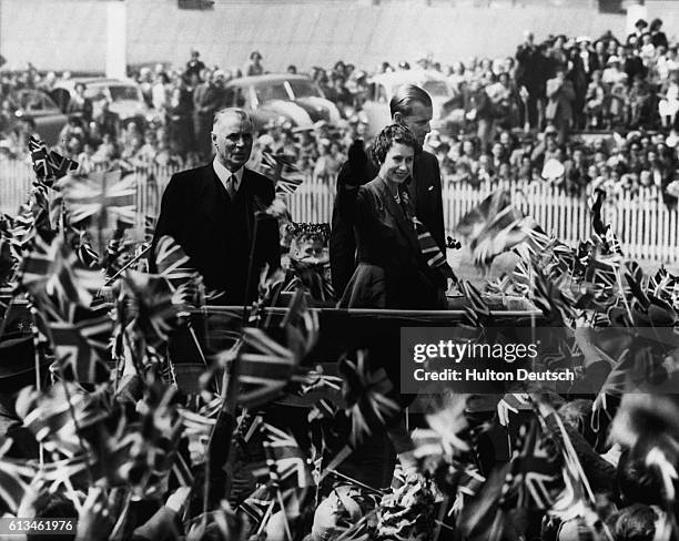 The Queen and the Duke of Edinburgh are cheered by a crowd of children waving flags at a picnic at Ferbury Park Racecourse, Dunedin, during their...