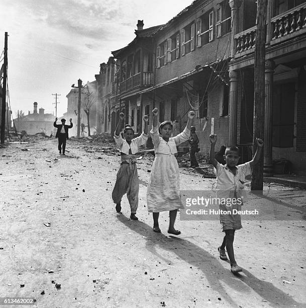 Korean children walk down a damaged street with their hands in the air, after US troops occupied the city of Inchon.