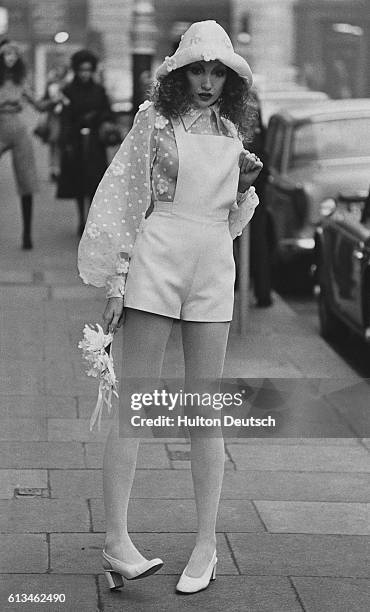 Young model sports a bridal outfit from the 1971 Diorling spring collection. She wears short, cotton, dungarees over an embroidered, organza blouse,...