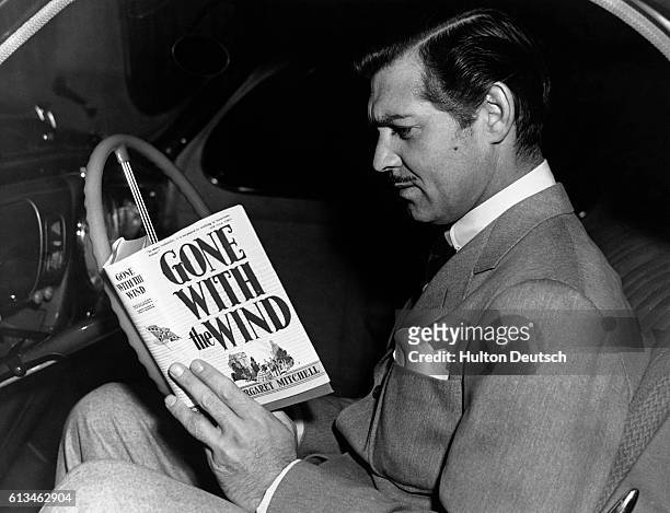 The actor Clark Gable, who played Rhett Butler in the 1939 film Gone with the Wind, reads a copy of the novel by Margaret Mitchell on which the film...