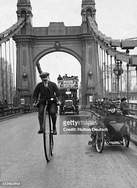 Man riding a penny-farthing bicycle over Hammersmith Bridge in London.