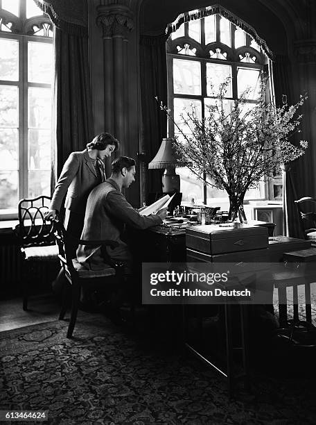 King George VI of England reads some royal papers, while his daughter Princess Elizabeth looks over his shoulder.