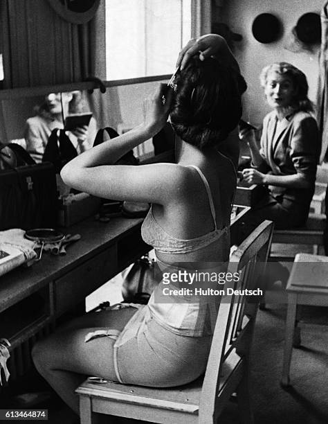Fashion model curls her hair while she chats backstage at a show in the Piguet Fashion House. Paris, 1946.