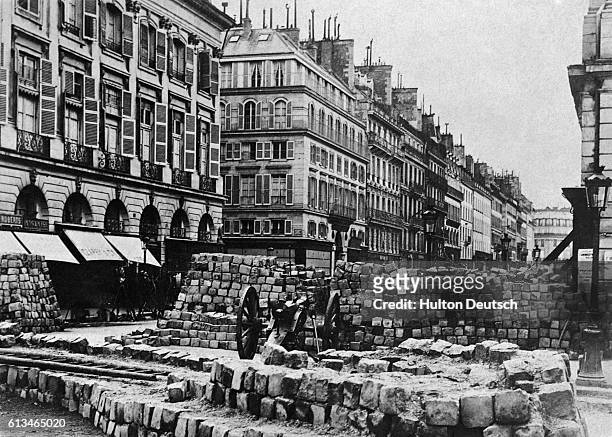 Paris street is barricaded with a stone-block wall and cannon, during the Franco-Prussian War or, just after, during the Paris Commune. Ca. 1870-1871.