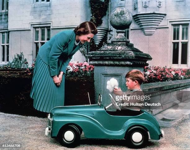 Queen Elizabeth watches her son Prince Charles driving in a toy car on the grounds of Balmoral Castle.