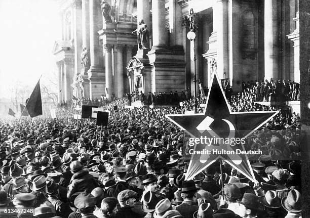 Huge crowd turns out for a Communist rally in Berlin. One person holds a large star-shaped placard emblazoned with a hammer and sickle. 1918.