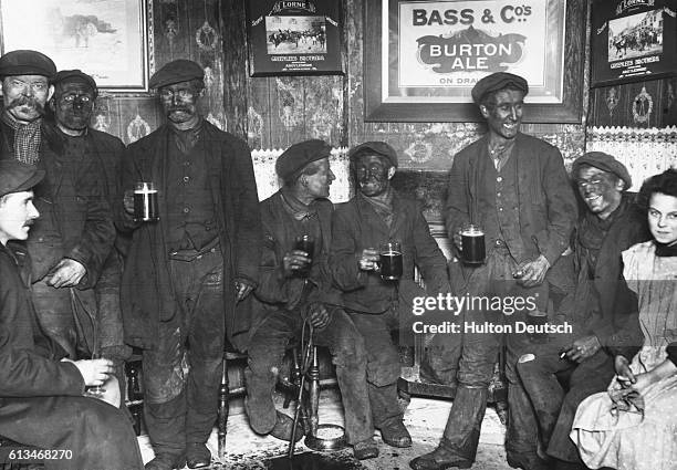 Group of coal miners, still dirty from the mines, discusses the impending coal strike over pints of beer at a local pub.