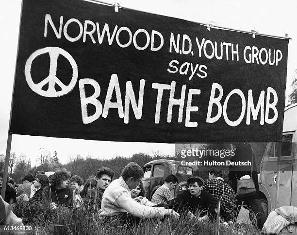 Group of anti-nuclear weapons protesters sit beneath a 'ban the bomb' banner at a protest.