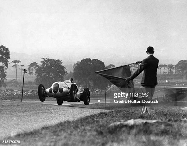 Race official waves a flag as Bernd Rosemeyer races past in his Mercedes-Benz racecar during the Donnington Park Grand Prix. Rosemeyer eventually won...