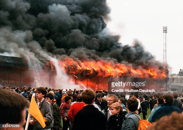 The stand burns while fans look on at Bradford football ground at the Valley Parade, Bradford in 1985. | Location: Valley Parade, Bradford, England.