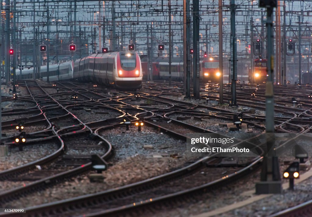 Commuter train approaching busy railway track field at twilight