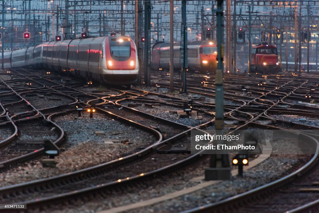 Commuter train approaching busy railway track field at twilight