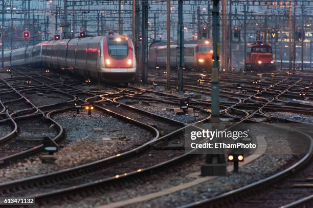 commuter train approaching busy railway track field at twilight - railroad crossing night stock pictures, royalty-free photos & images