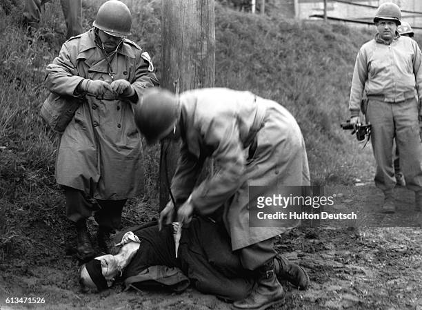 United States Army physicians examine the body of Richard Jarczyk to be sure that he is dead after execution by a firing squad in Germany in 1945....