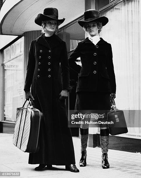 Two young women model outfits designed by Joan Langberg for the Dior London Autumn Collection. One wears a long brown velour coat, worn over a tunic...