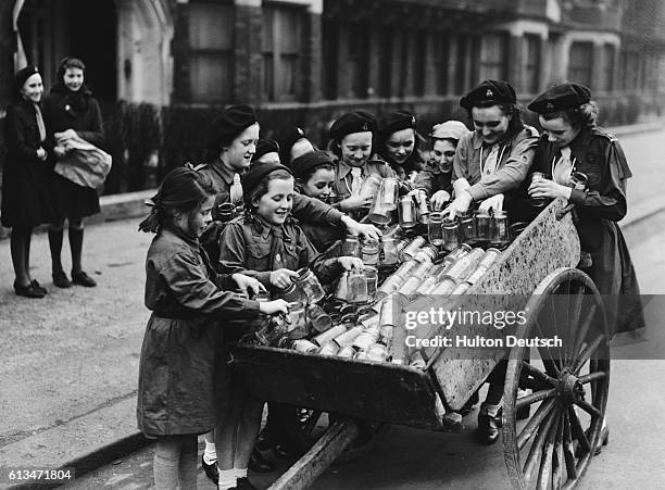 Brownies and Guides of the 14th Battersea Park group stand with the cart containing the jars they have collected. Boy Scouts and Girl Guides have...