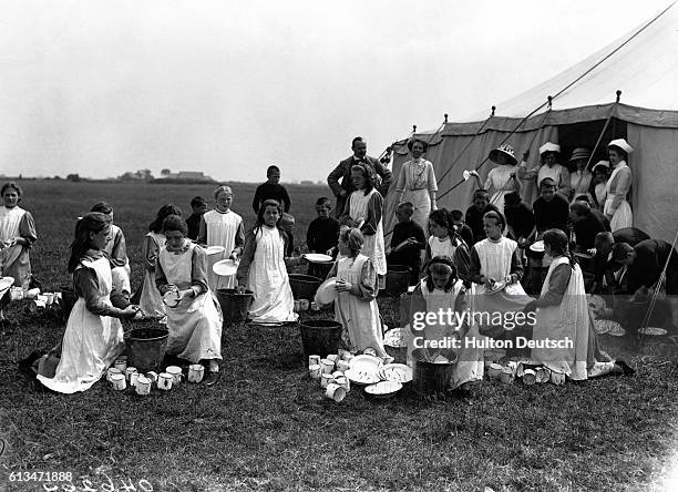 Orphaned children from the Islington workhouse wash cups and plates outside their tent in a field on Canvey Island. July, 1912.