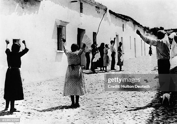 Inhabitants of Castilblanco de Los Arroyos raise their arms in gestures of surrender as Nationalist troops move into their village, during the...