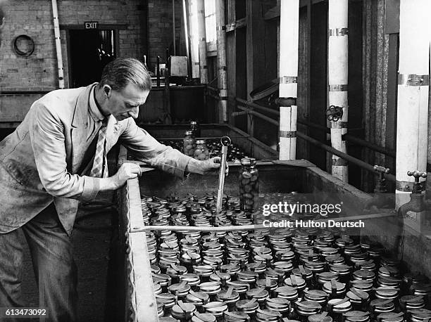 Food processing worker measures the temperature of the bottled plums at a canning factory. | Location: Winchcome, Glostershire, England, UK.