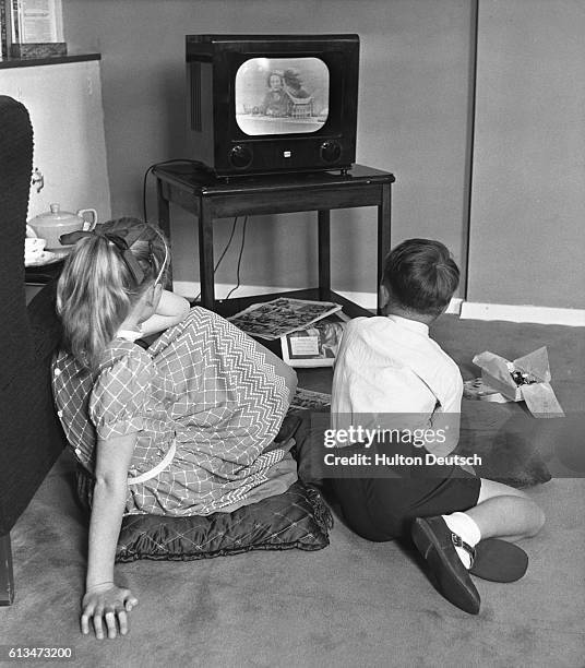 Young brother and sister watch television at home.