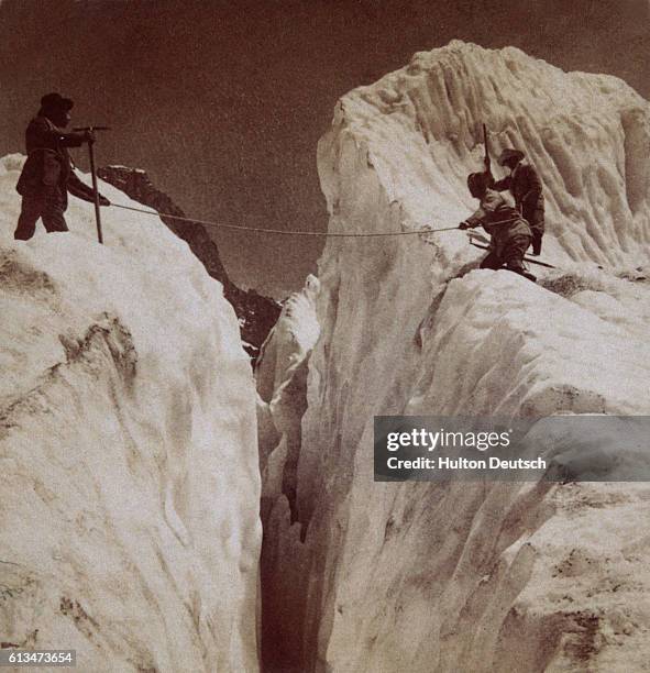 Three men attempt to cross a crevasse in the Alps.