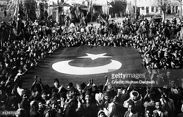 Crowd surrounds a giant Turkish flag during celebrations following the departure of occupying French troops from the southern Turkish city of Adana...