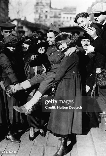 Civilian women celebrate the end of World War I by carrying a soldier in their arms.