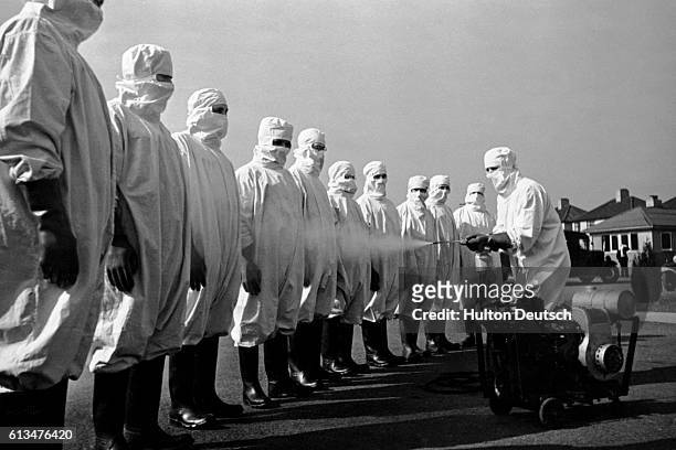 Group of people wearing protective suits are sprayed with a substance, possibly a disinfectant, to prevent the spread of typhus.