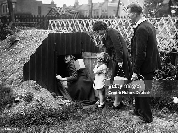 Family, each carrying their gas masks in a little box, enter the dug-out air raid shelter in their garden, 1939.