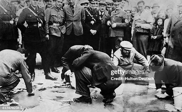 Young German people watch elderly Jewish men scrub the streets.