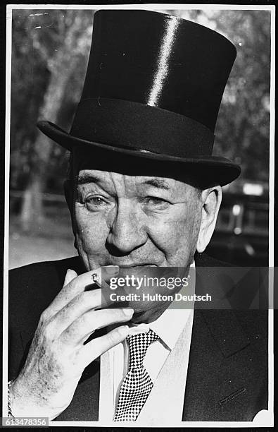 Noel Coward smokes a cigarette after the Queen awards him with a knighthood.