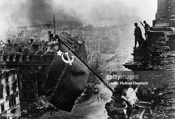 Soldier flies a Soviet flag over the Reichstag after the fall of Berlin to Soviet forces in 1945.