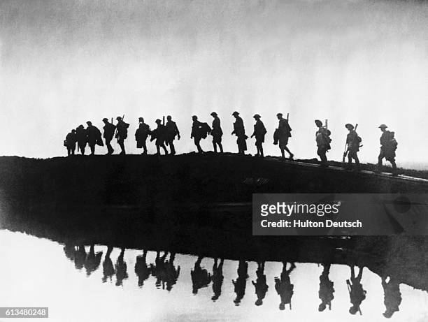 An East Yorkshire regiment of British troops in silhouette negotiate their way around a rainwater-filled shell crater near the Western Front during...