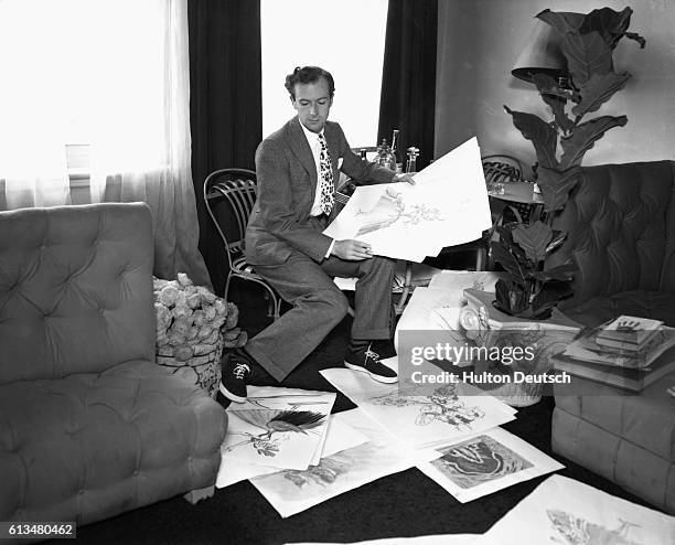 Cecil Beaton , the English photographer, and theatrical designer, examines costume designs at his home.