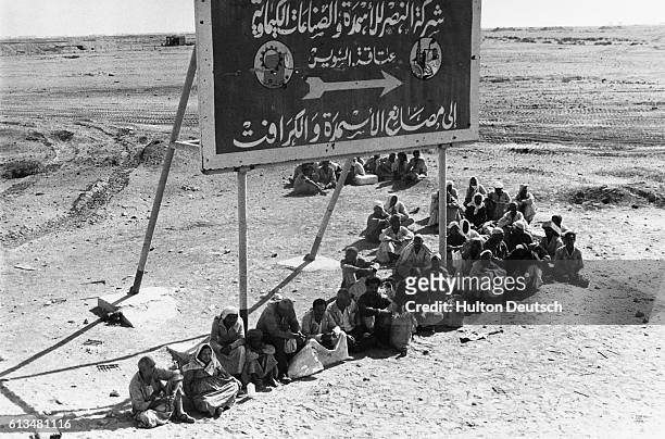 Group of refugees and evacuees sits under a billboard in the middle of the desert, displaced by the Yom Kippur War against Israel.