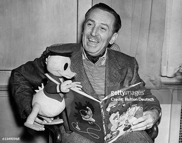 Film producer and cartoonist Walt Disney with a toy Donald Duck reading Alice in Wonderland, 1951.
